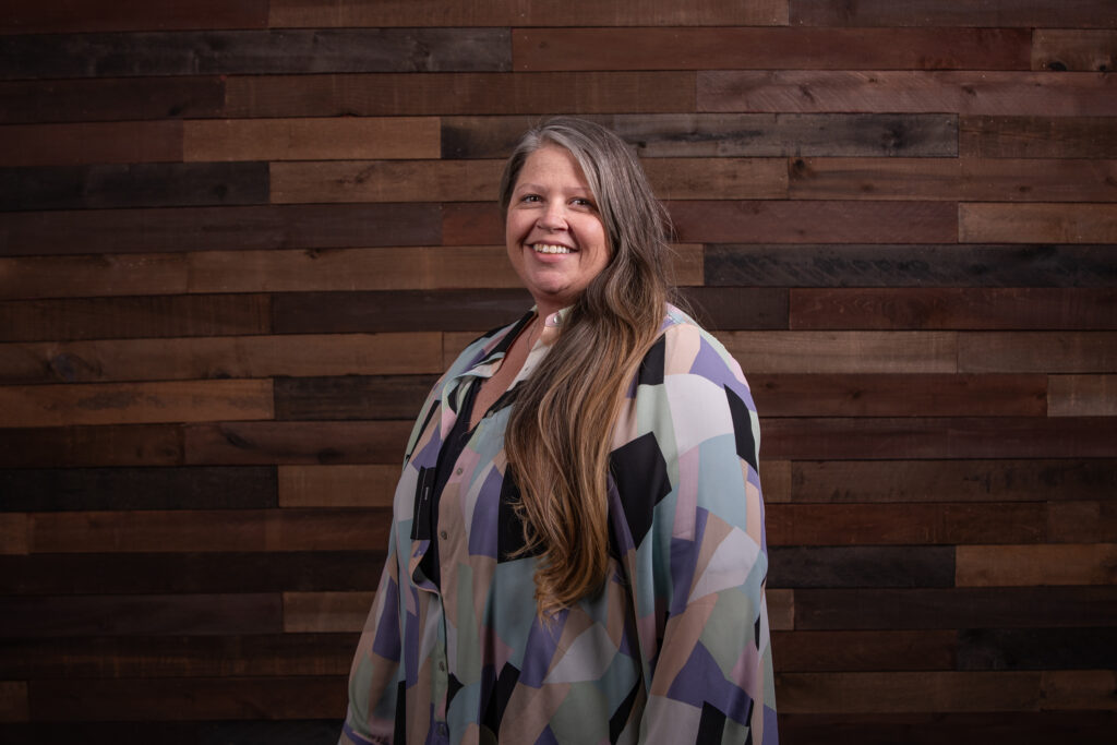 woman in a multi-colored blouse in front of a wooden background