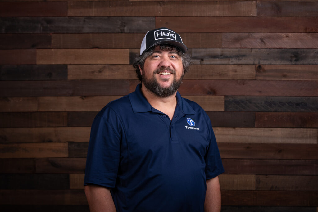 man with a beard and a black hat wearing a navy polo in front of a wooden background