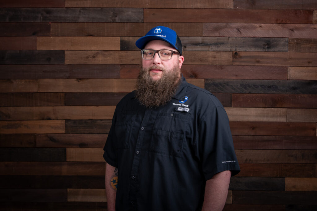 man with a long beard and a blue hat wearing a black polo in front of a wooden background