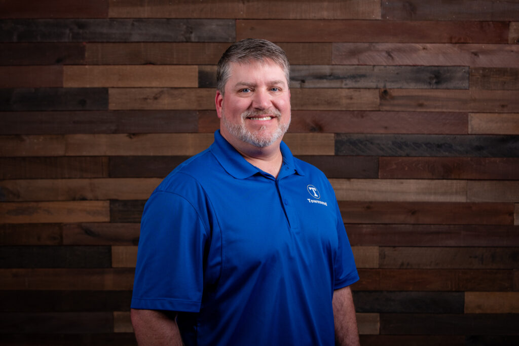 man with a blue polo and a beard in front of a wooden background