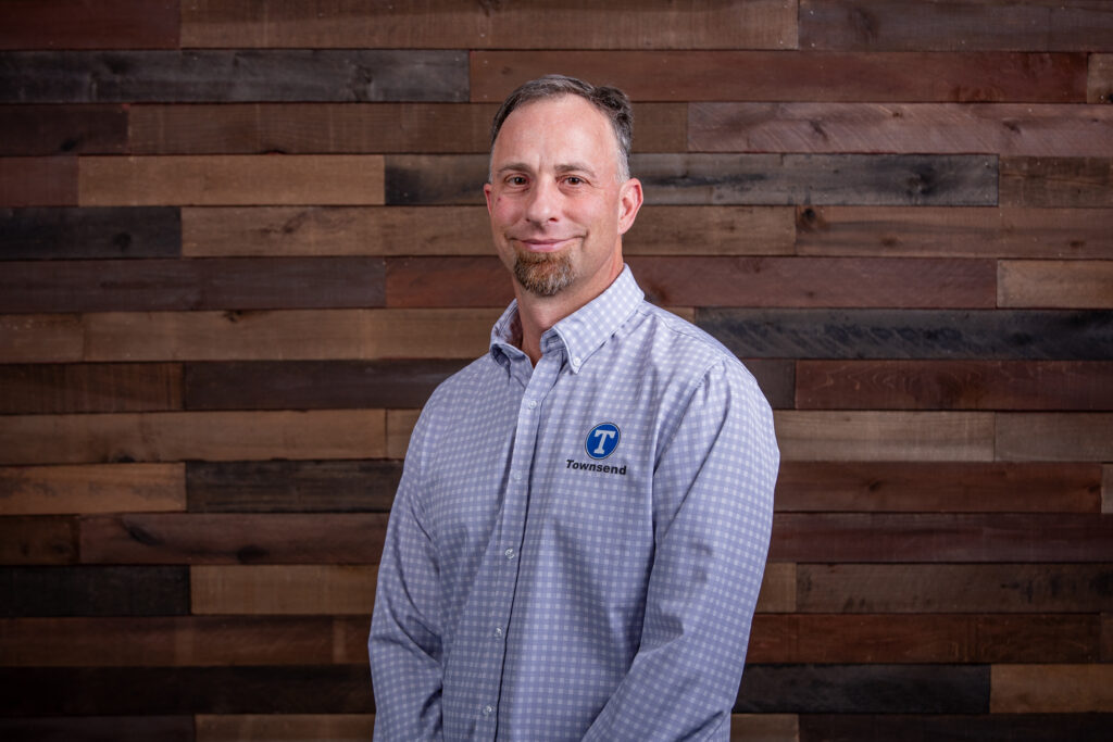man with a beard and wearing a light blue button up shirt in front of a wooden background