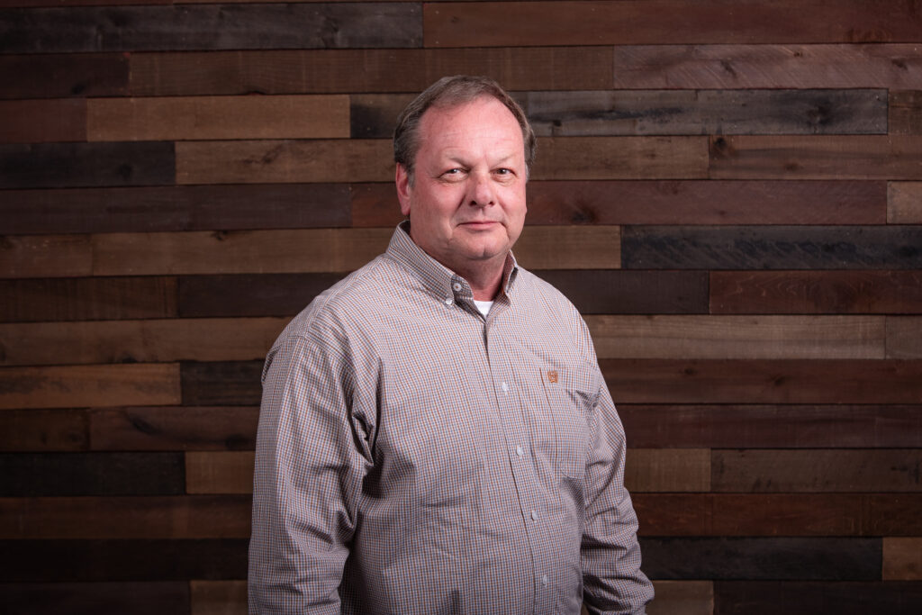 man with a light brown button up shirt in front of a wooden background