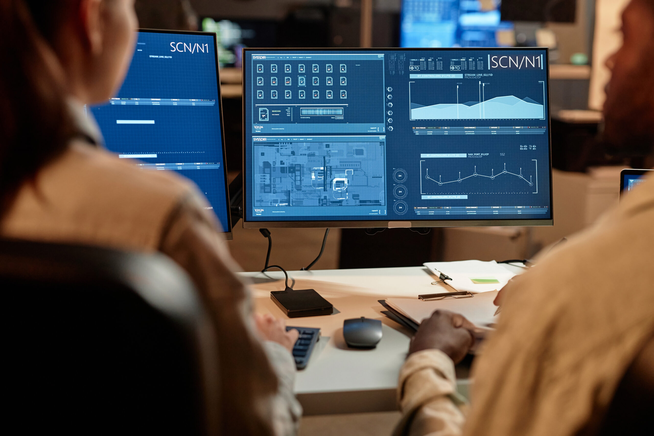 Looking over the shoulders of two developers analyzing charts on two computer screens