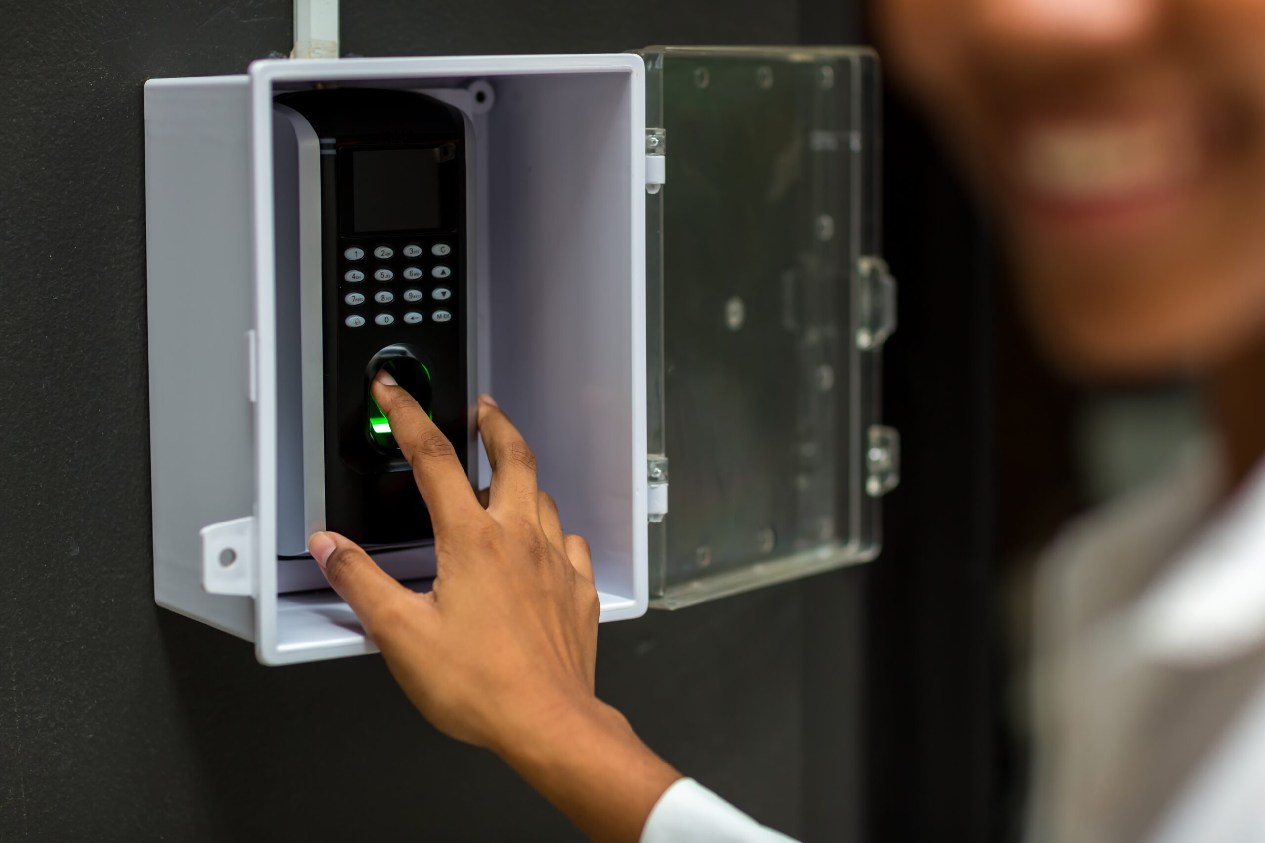 close up of a hand putting a finger onto a black and white finger print detector that is on a grey wall