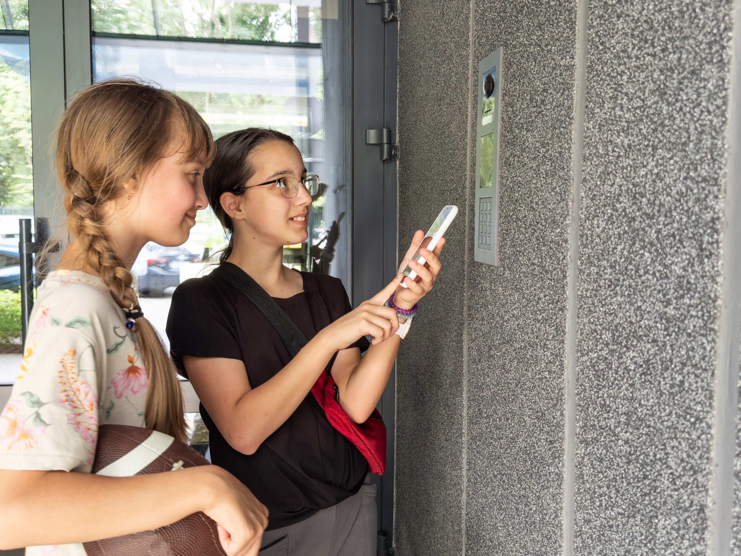 Two teenage girls with braids using their cell phone for wireless entry at an office building door