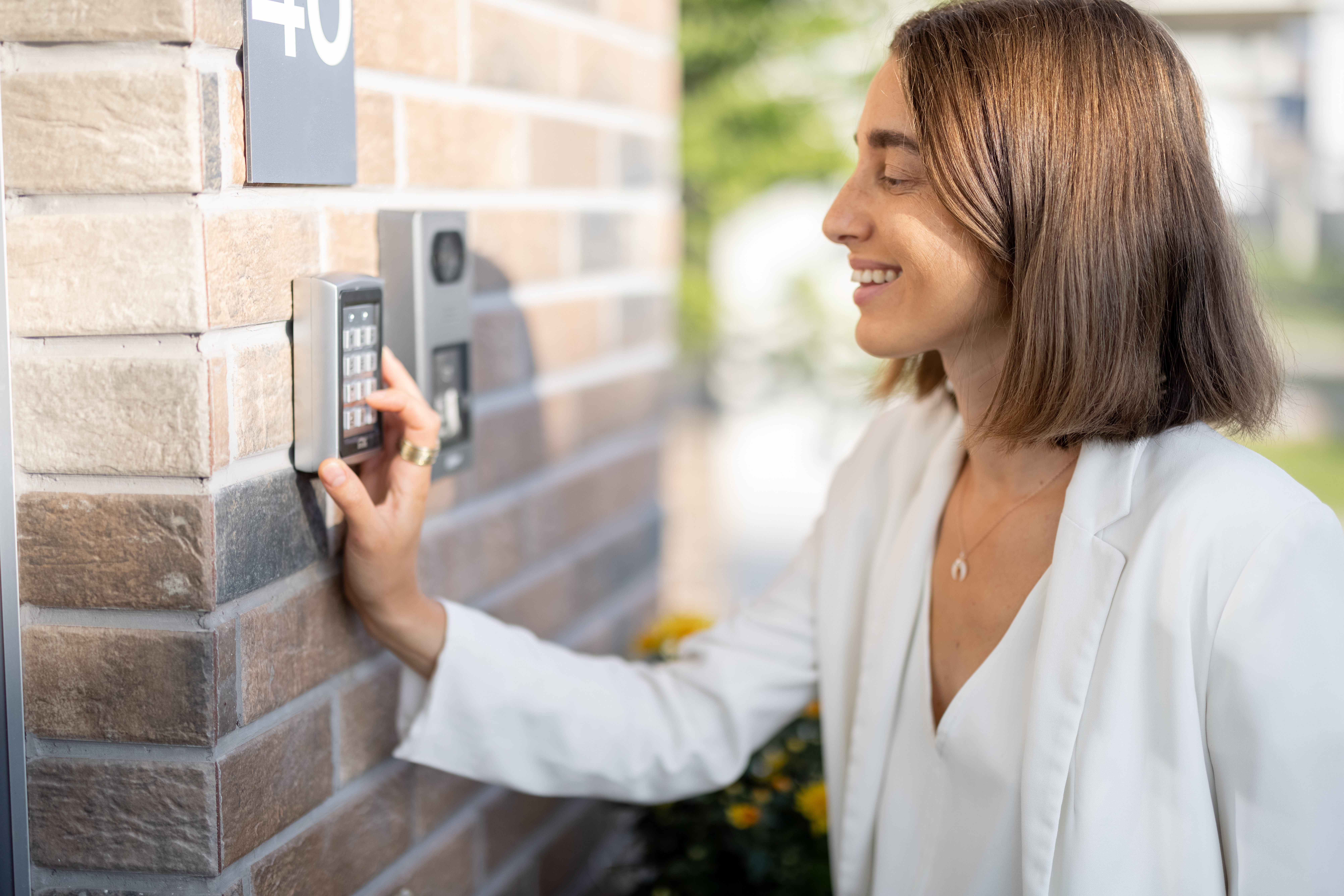 Woman with short, dark hair wearing a white blazer entering a code on a keypad mounted on a brick wall