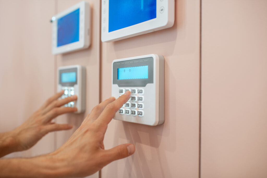 White male hand pushing the buttons on a home alarm keypad that is mounted on a pink wall