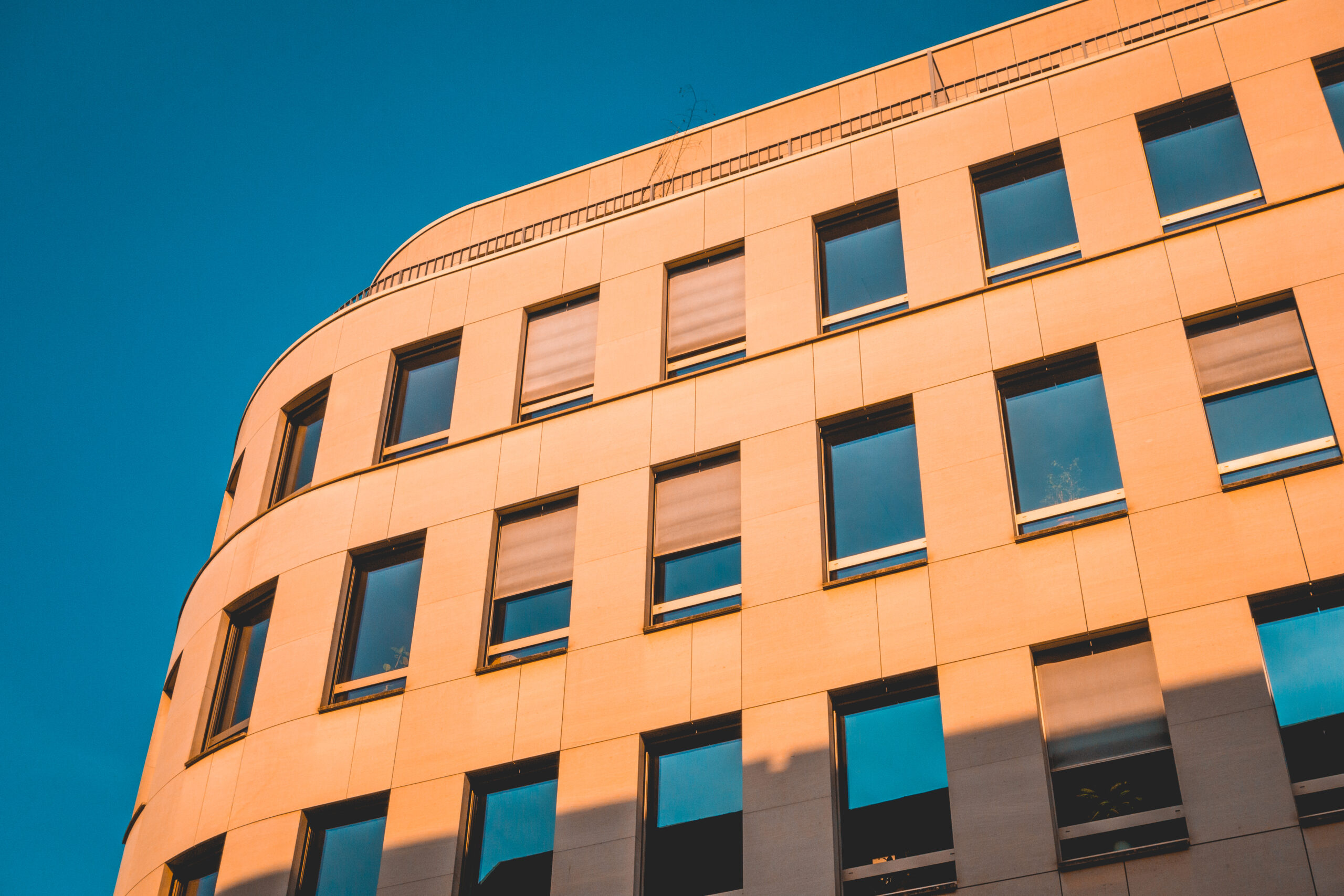 Modern curved art deco building with windows colored orange from the sunset with bright blue sky
